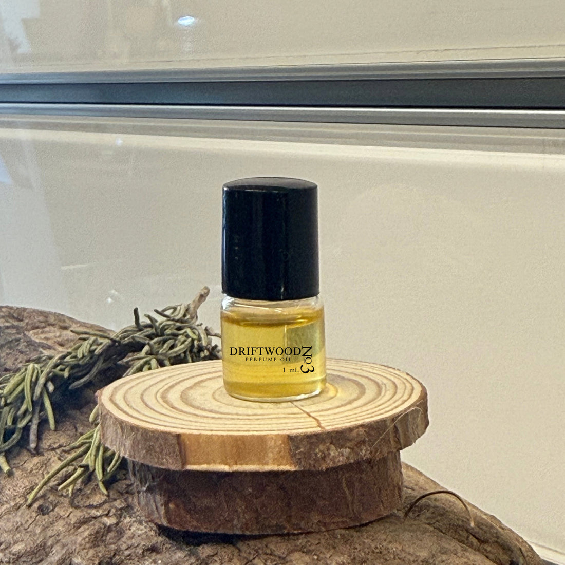 Small bottle of Driftwood No3 perfume on wood with rosemary and a light background