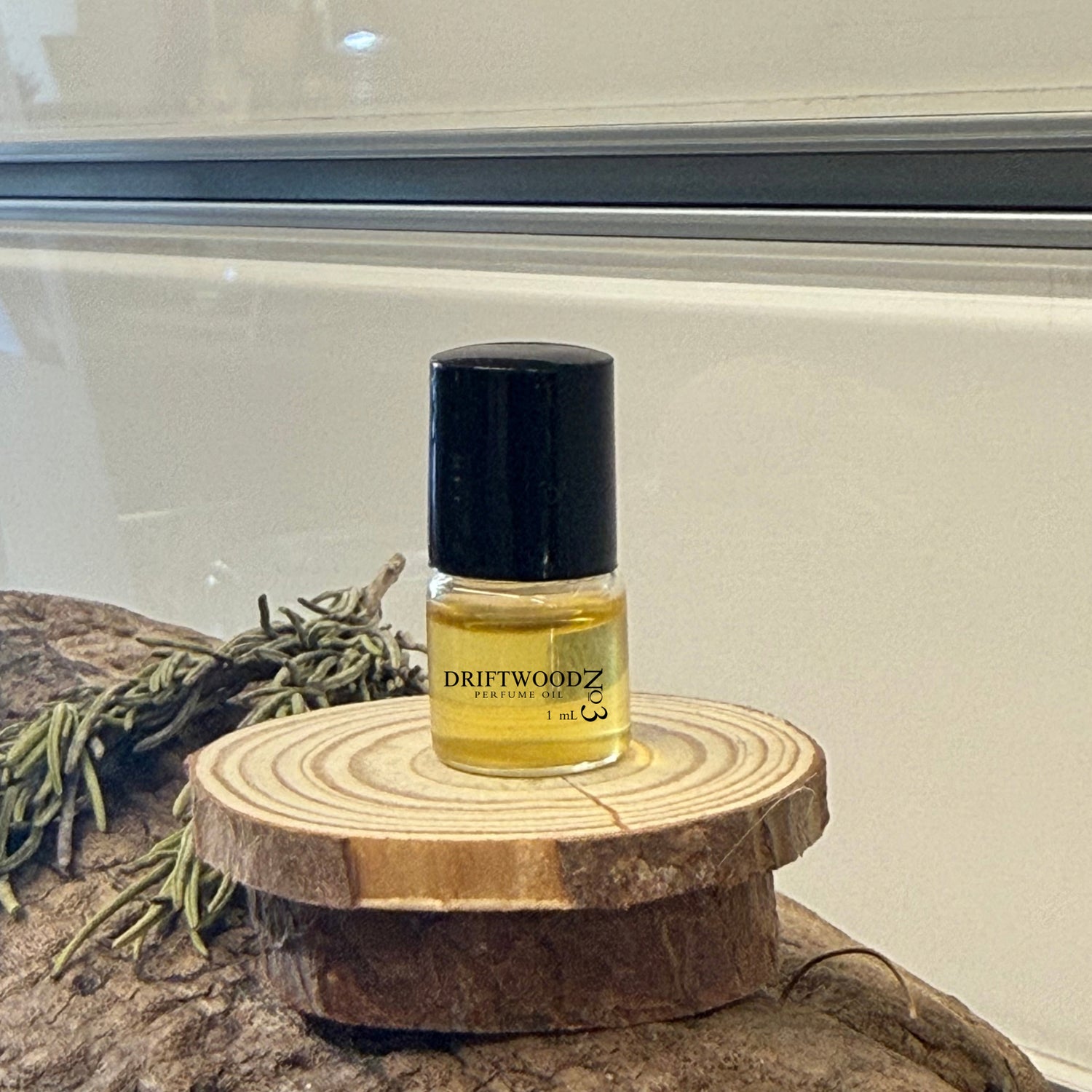 Small bottle of Driftwood No3 perfume on wood with rosemary and a light background